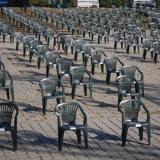 Foto: Adrian Bancu; Quelle: Pexels Zahlreiche dunkelgraue Monoblock-Stühle aus Kunststoff stehen in regelmäßigen Reihen auf einer gepflasterten Fläche im Freien.