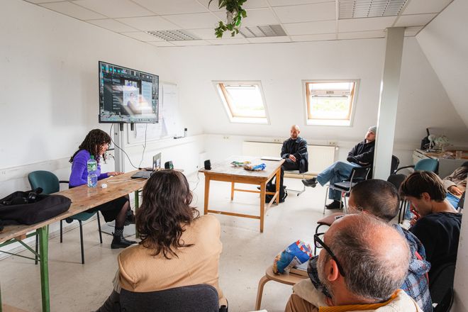 Projekt »Biennal of Care«, Foto: Julian Linden eine Person stellt ihr Projekt über einen Monitor vor einem Publikum vor