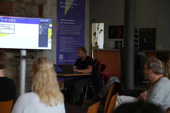 Illustrator Matthias Seifert als Live-Zeichner bei der Podiumsdiskussion »Was sind Umwelten«?, Foto: Leila Keivan Illustrator Matthias Seifert zeichnet live bei der Podiumsdiskussion mit, das Publikum kann über einen großen Monitor verfolgen, was er gerade zeichnet