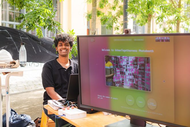 Projekt »Inviting Environments«, Foto: Julian Linden eine Person sitzt am Rechner der summaery-Fotobox und lacht in die Kamera