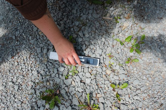 Projekt »PostCompost«, Foto: Julian Linden eine Person, die ein Messgerät auf den Schotterboden hält