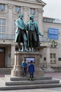 Das Foto zeigt das Goethe-und-Schiller-Denkmal auf Weimars Theaterplatz. Die metallene Gedenktafel zu Füßen der beiden Dichter wurde mit einem Plakat verhängt. Das Plakat trägt die Aufschrift: In Weimar gibt es mehr als 200 Gedenktafel. Nur 24 davon sind Frauen gewidmet.