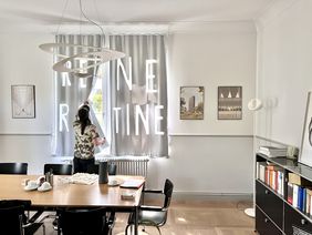»Liebe in Zeiten der Bürokratie« relocates the classic exhibition space to the offices of administrative staff at the Bauhaus-Universität Weimar. Photo: Benedict Thiele A person attaches a work of art to a curtain rail in an office space