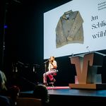 Laura Wiemers während einer Lesung im Rahmen der Preisverleihung am 21. September 2025 in Paderborn; Foto: VerbundVolksbank OWL eG Laura Wiemers sitzt auf einer Bühne und hält ein Buch in der Hand, aus dem sie liest