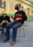 A senior VR user with a head-mounted display, sitting on a chair is instructed.