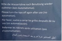 Foto eines Schildes mit der Aufschrift »Bitte die Wasserhähne nach Benutzung wieder zudrehen (kein Automatismus)« in fünf Sprachen übersetzt.