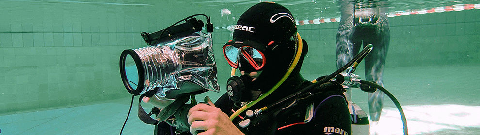 Ein Studierender mit Tauchanzug, Sauerstoffflasche und Unterwasserkamera in einem Schwimmbecken.